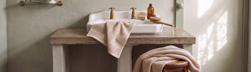 Baño estilo spa con toallones de algodón apilados y luz cálida.
